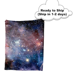 Puede incluir: Una manta suave y mullida con un estampado de galaxia vibrante con nebulosas giratorias y estrellas brillantes en tonos azules, morados y rosas.