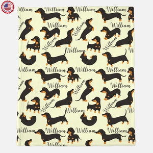 Puede incluir: Una tela de color crema con un patr&oacute;n repetido de perros salchicha negros. Cada perro tiene una franja marr&oacute;n en la espalda y el nombre "William" est&aacute; escrito debajo de cada perro.