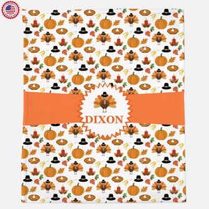 Puede incluir: Una manta de bebé blanca con temática de Acción de Gracias. La manta presenta un patrón repetitivo de pavos, calabazas, pasteles y velas. La manta tiene una pancarta naranja personalizada con el nombre "DIXON" en un estallido de estrella blanco.