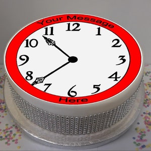 May include: A white cake with a red border and a clock face design. The clock face has black numbers and hands. The text "Your Message Here" is printed around the clock face.