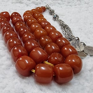 May include: A brown amber prayer beads necklace with a silver tassel and silver charms. The beads are round and have a glossy finish.