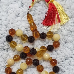Puede incluir: Un collar de cuentas de ámbar con un borla. Las cuentas son una mezcla de marrón, amarillo y blanco.