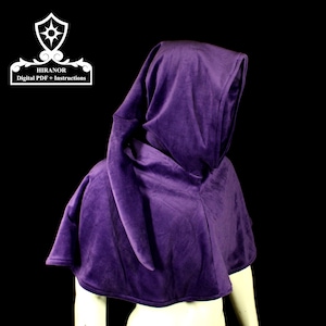 Può includere: Un mantello con cappuccio viola con una lunga coda fluente. Il cappuccio è tirato sopra la testa e il mantello è drappeggiato sulle spalle.