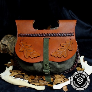 Könnte beinhalten: Eine handgefertigte Ledertasche mit einem braunen Lederteil und einem grünen Wildlederboden. Die Tasche hat zwei Eichenblatt-Designs und einen geflochtenen Riemen. Ein grüner Riemen mit Metallschnalle sichert die Tasche.