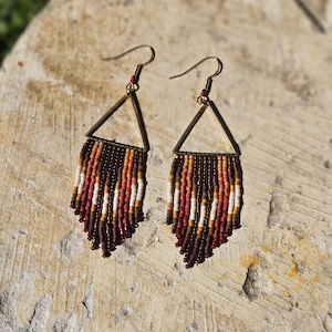 May include: A pair of dangle earrings with a triangular frame and a fringe of brown, red, white, and beige beads.