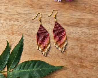 May include: A pair of long, beaded earrings with a gradient of red, orange, and yellow beads. The earrings are hanging from gold hooks.