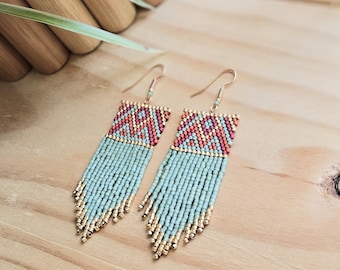 May include: A pair of long, beaded earrings with a geometric pattern in shades of green, red, and gold. The earrings are hanging from gold hooks.