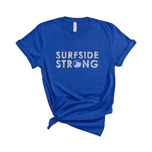May include: Royal blue t-shirt with the text "SURFSIDE STRONG" in white with a blue wave graphic in the "O".