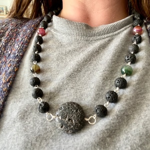 May include: A black lava rock necklace with silver chain accents and colorful agate beads. The necklace features a large lava rock pendant.