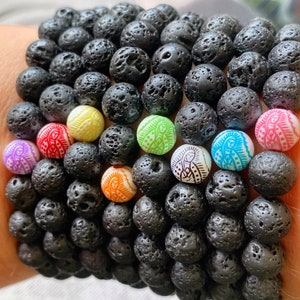 Könnte beinhalten: Ein Stapel schwarzer Lava-Armbänder mit bunten Perlen, die ein religiöses Bild zeigen. Jede Perle hat eine andere Farbe und ein anderes Design.