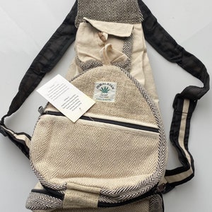 May include: A beige hemp backpack with black straps and a black and white chevron pattern. The backpack has two zippered pockets and a small pocket on the front. The tag on the backpack reads "Himalayan Hemp Textile Made in Nepal".