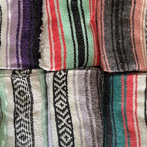 May include: A collection of six folded woven blankets featuring various striped patterns. The blankets display a range of colors including purple, white, mint green, coral, black, grey, and teal, with some sections showcasing intricate geometric diamond motifs.