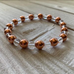 Pode incluir: Um bracelete feito com contas de quartzo transparente e cobre alternadas.
