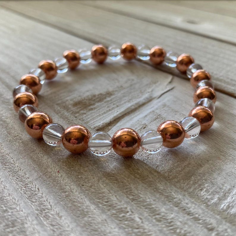 Pode incluir: Um bracelete feito com contas de quartzo transparente e cobre alternadas.