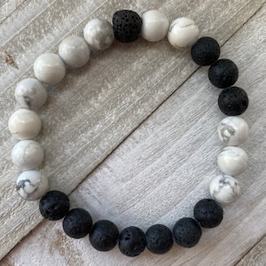 Peut inclure: Un bracelet composé de perles blanches et noires. Les perles blanches sont en howlite blanche et les perles noires en lave.