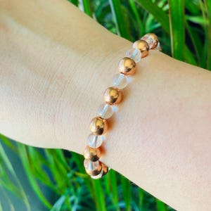Pode incluir: Um bracelete feito de contas transparentes e douradas rosadas. O bracelete est&aacute; no pulso de uma pessoa.