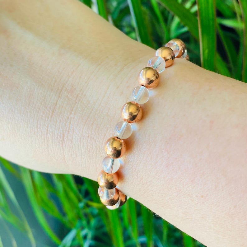Pode incluir: Um bracelete feito de contas transparentes e douradas rosadas. O bracelete est&aacute; no pulso de uma pessoa.