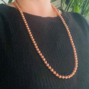 May include: A long copper necklace with round beads. The necklace is worn by a person, but the person's face is not visible.