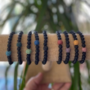 May include: A set of eight black lava stone bracelets with colourful lava stone beads. Each bracelet has a different coloured bead.