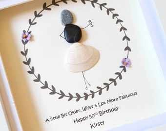May include: A framed artwork with a whimsical design. The artwork features a figure made of stones and a seashell, holding a drink. The text reads: "A little Bit Older, Wiser & Lot More Fabulous Happy 50th Birthday Kirsty".