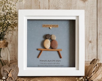 May include: A square white framed wall art piece featuring pebble art of two figures sitting on a wooden bench against a blue background with white stars. The text reads: Sharon & Tiffany, Friend's Are like stars, You don't always see them, But you know they're always there.