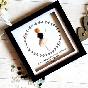 Pu&ograve; includere: Opera d'arte incorniciata con una figura fatta di conchiglie e pietre, che tiene un palloncino. La figura &egrave; circondata da una ghirlanda, con il testo: "A little Bit Older, Wiser + Lot More Fabulous Happy 50th Birthday Mum."