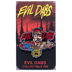 May include: A red, yellow, and blue enamel pin featuring a cartoon character with a bloody face and the text "Evil Dabs" in red and yellow. The pin is on a black card with the text "Evil Dabs Collectible Pin" in white.