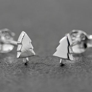 May include: A pair of silver stud earrings featuring a small, detailed tree design.