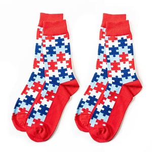 Könnte beinhalten: Ein Paar rote Socken mit einem Muster aus blauen, weißen und hellblauen Puzzle-Teilen.