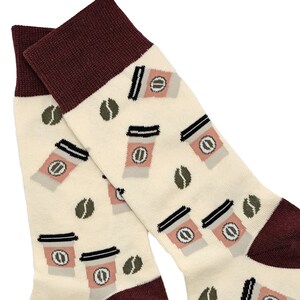 Könnte beinhalten: Ein Paar weiße Socken mit einem braunen und rosafarbenen Kaffeetassen-Design. Die Socken haben einen dunkelroten Bund.