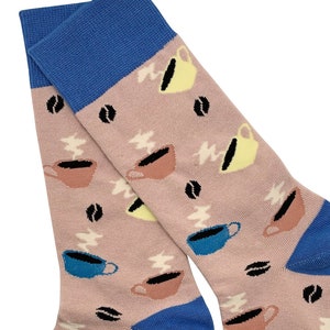 Könnte beinhalten: Ein Paar rosa Socken mit blauem Bund. Die Socken haben ein Muster aus Kaffeetassen mit Dampf und Kaffeebohnen.