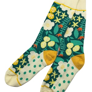 Può includere: Un paio di calzini verdi, bianchi e gialli con un motivo floreale. I calzini hanno un polsino color crema con una striscia gialla.