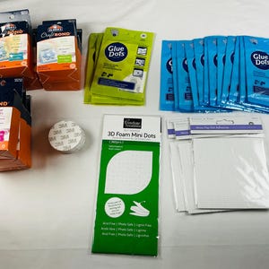 May include: A collection of adhesive craft supplies including multiple boxes of Elmer's Craft Bond glue spots, a roll of 3M adhesive, several packs of Glue Dots in blue and green packaging, and a package of Couture Creations 3D foam mini dots.