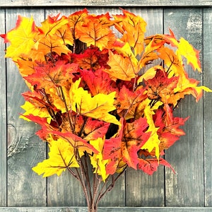 May include: A bouquet of fall leaves in shades of red, orange, and yellow. The leaves are arranged in a cluster and have a rustic, natural look.
