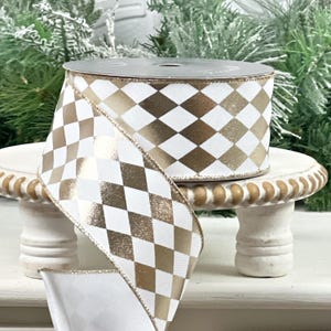 May include: A spool of decorative ribbon with a white and gold harlequin pattern. The ribbon is displayed on a small, white, decorative stand. The ribbon is ideal for gift wrapping, crafting, or holiday decorations.