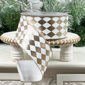 May include: A roll of white ribbon with a gold harlequin pattern. The ribbon is displayed on a small, white, decorative stand. The ribbon is ideal for gift wrapping, crafting, or holiday decorations.