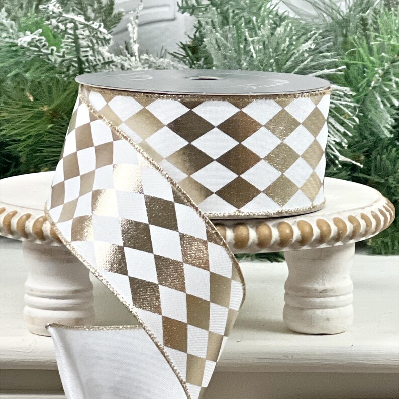 May include: A spool of decorative ribbon with a white and gold harlequin pattern. The ribbon is displayed on a small, white, decorative stand. The ribbon is ideal for gift wrapping, crafting, or holiday decorations.
