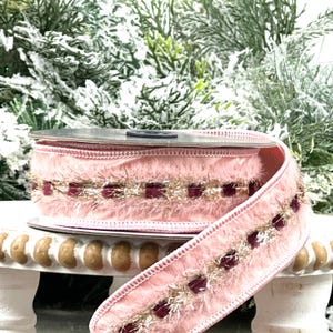 Puede incluir: Un rollo de cinta rosa con una textura suave y aterciopelada. La cinta está adornada con oropel dorado y acentos cuadrados burdeos. Ideal para manualidades y proyectos decorativos.