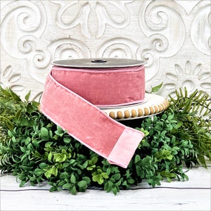 A roll of 2.5" pink velvet ribbon sits upon a white wood pedestal surrounded by greenery.