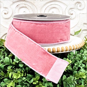 A roll of 2.5" pink velvet ribbon sits upon a white wood pedestal surrounded by greenery.