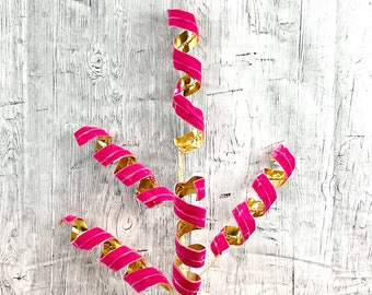 May include: Pink and gold curly ribbon streamers on a white wood background.