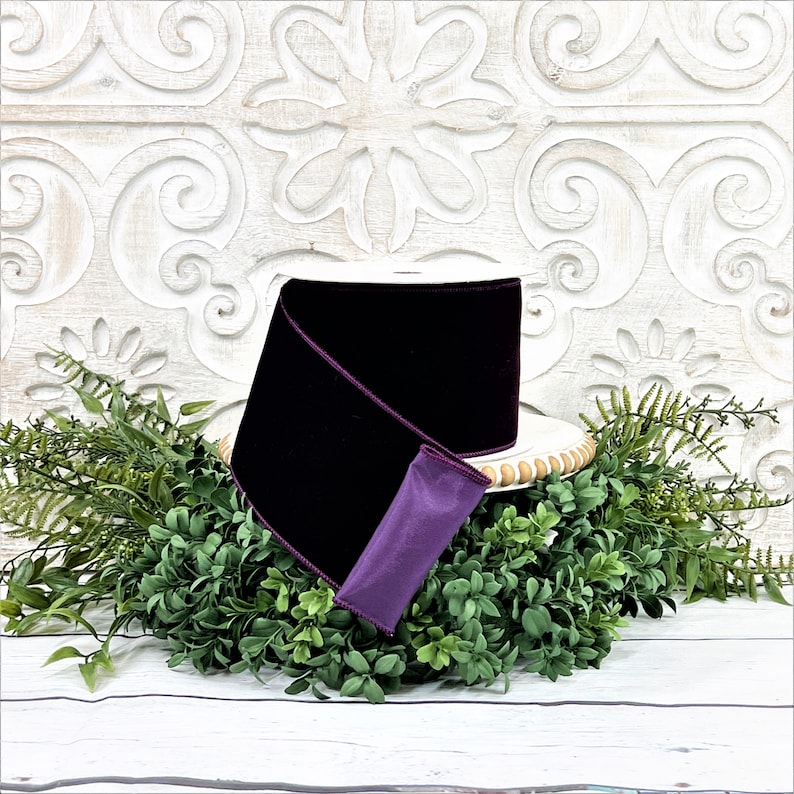 A 4" roll of dark purple velvet sits on a white wood pedestal surrounded by greenery.