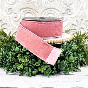 A roll of 2.5" pink velvet ribbon sits upon a white wood pedestal surrounded by greenery.