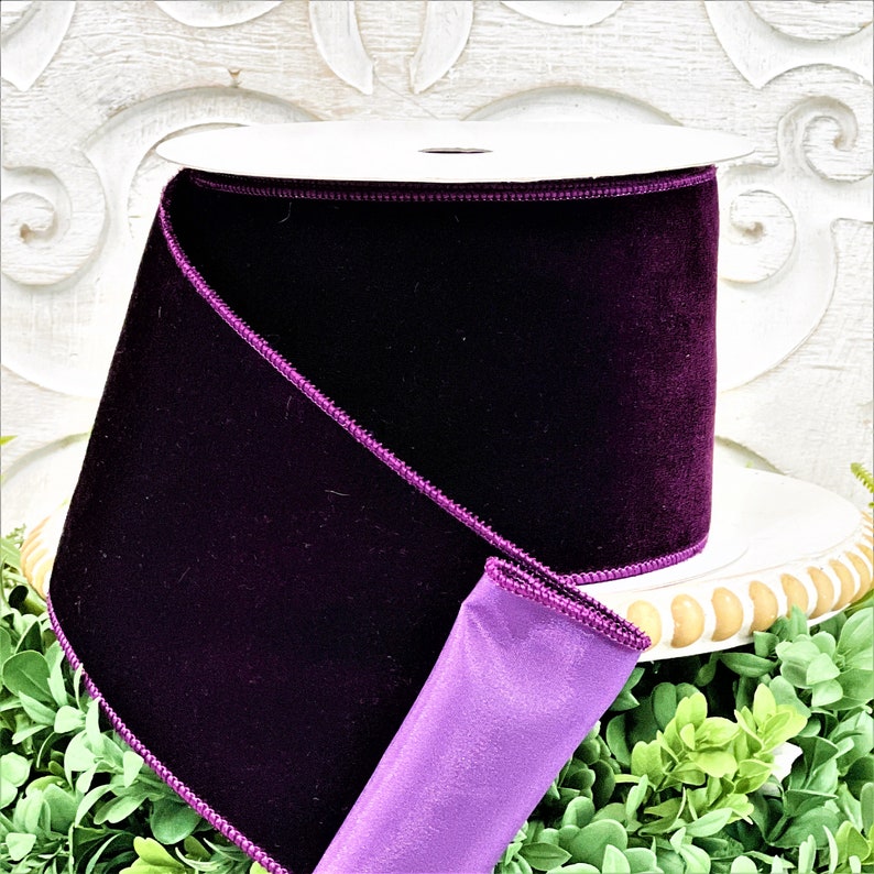 A 4" roll of dark purple velvet sits on a white wood pedestal surrounded by greenery.