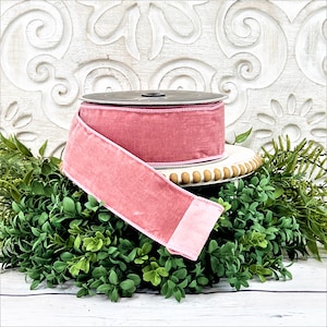 A roll of 2.5" pink velvet ribbon sits upon a white wood pedestal surrounded by greenery.