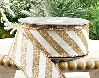 May include: A spool of white and gold striped ribbon. The ribbon has a diagonal stripe pattern with a glittery gold finish. The ribbon is on a white spool and is suitable for crafts and gift wrapping.