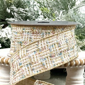 Könnte beinhalten: Eine Rolle dekoratives Band mit einem gewebten Tweed-Muster. Das Band hat einen cremefarbenen Hintergrund mit goldenen, blauen und roten Flecken. Die Kanten sind mit goldenem Metallic-Garn verziert. Geeignet für Bastelarbeiten und Geschenkverpackungen. Die Bandbreite beträgt ca. 6,35 cm.