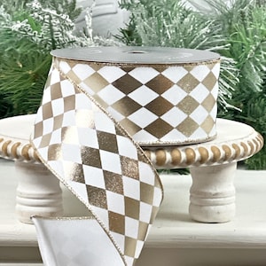 May include: A spool of decorative ribbon with a white and gold harlequin pattern. The ribbon is displayed on a small, white, decorative stand. The ribbon is ideal for gift wrapping, crafting, or holiday decorations.