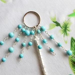 Puede incluir: Un llavero de plata con un dije de plata y múltiples hebras de cuentas turquesa.