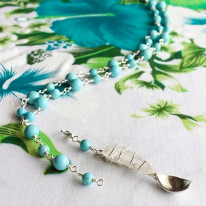 May include: A turquoise gemstone necklace with a silver chain and a pendant featuring a clear quartz crystal wrapped in silver wire and a silver spoon.